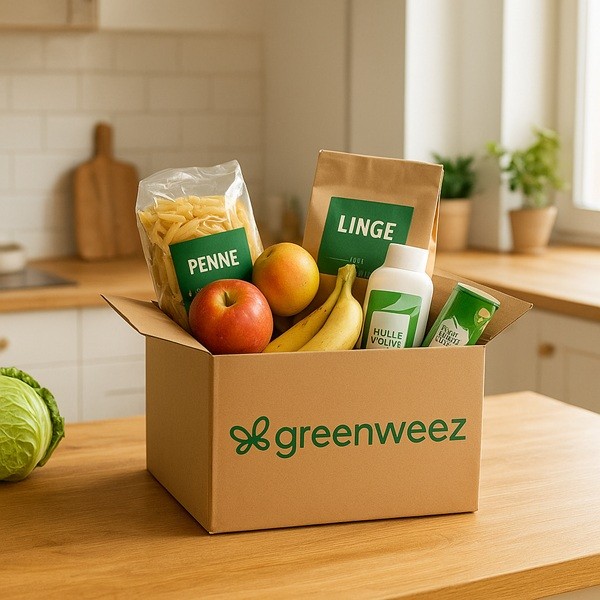 Carton Greenweez ouvert sur une table de cuisine avec pâtes bio, fruits, produits ménagers écologiques et huile, illustrant des courses éco-responsables à domicile.