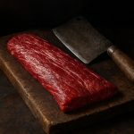 Hampe de bœuf crue persillée posée sur un billot de bois avec un couteau de boucher ancien, morceau traditionnel au goût intense.