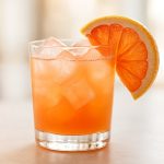 Cocktail rafraîchissant au pink grapefruit avec glaçons et tranche de pamplemousse rose.