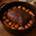 Épaule de chevreuil au four en cuisson lente dans une cocotte en fonte avec pommes de terre, carottes et oignons rôtis.